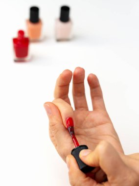 Beyaz masanın önüne kırmızı oje sürerken yakın plan kadın eli.