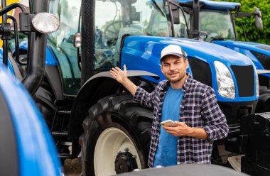 Cep telefonu tutan ve malzeme galerisindeki yeni traktöre işaret eden erkek tarım işçisi.