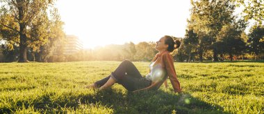 Huzurlu bir kadın arka planda çayır olan yeşil çimlerde dinleniyor.