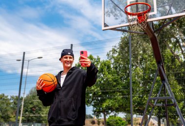 Sokak basketbolu sahasında akıllı telefondan fotoğraf gönderen genç bir kadın.