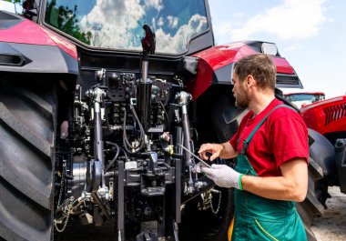 Kırsal alanda dijital tablet kullanan erkek tamirci tarla traktörünü kontrol ediyor