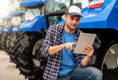Dijital tablet kullanan bir adam dışarıda traktör kullanıyor.