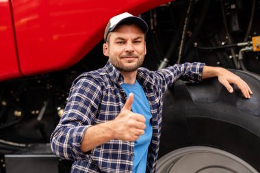 Erkek tarım işçisi, tarım malzemelerinin yanında onaylı jest gösteriyor. Baş parmağını kaldıran adam..