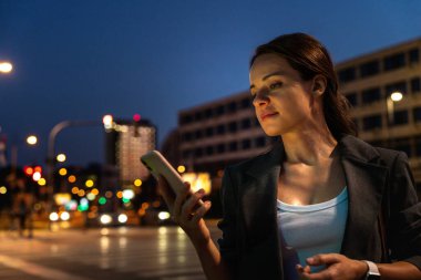 Şehir ışıkları açık havada akıllı telefon kullanan bir kadın.