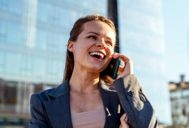 Şehir caddesinde cep telefonuyla konuşan neşeli şehirli kadın