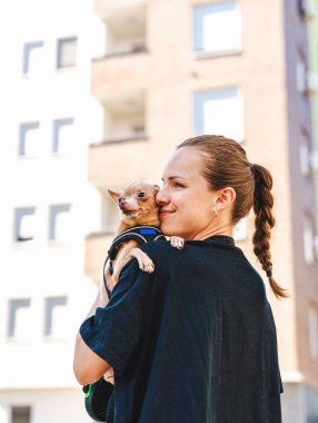 Dışarıda yürürken küçük köpeğini kucaklayan bir kadın. Oyuncak Teriyer Köpeği. Evcil hayvanlarla hayat.