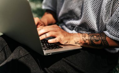 Açık havada dizüstü bilgisayarda çalışan dövmeli kadın elleri.