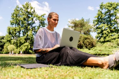 Bayan öğrenci ya da serbest çalışan biri yaz parkında laptopta çalışıyor.
