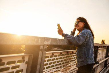 Şehirdeki genç bir kadın köprüde akıllı telefonunu kullanıyor..