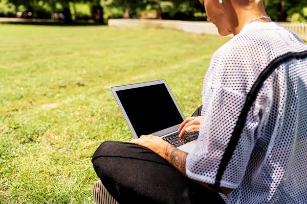 Şehir parkında dizüstü bilgisayar kullanan bir kadın.