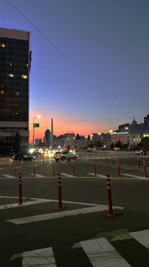  Kyiv şehir manzarası gün batımı gökyüzünü aydınlatıyor. Arabalar yol ayrımcılarıyla işaretlenmiş yoğun bir kavşaktan geçer, binalar arka planı oluşturur..