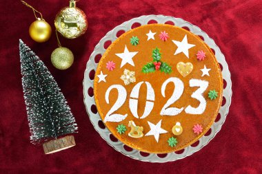 Traditional Greek new years cake, known as vasilopita, for 2023 and Christmas ornaments on red velvet background clipart