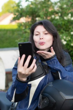Genç, güzel, esmer motorcu arkadaşlarıyla cep telefonunda sohbet ediyor, kaliteli bir fotoğraf. Yüksek kalite fotoğraf