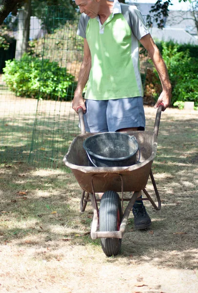 gardener man in dirty work clothes, rolls a rusty cart with a bucket, spring work in the garden. High quality photo