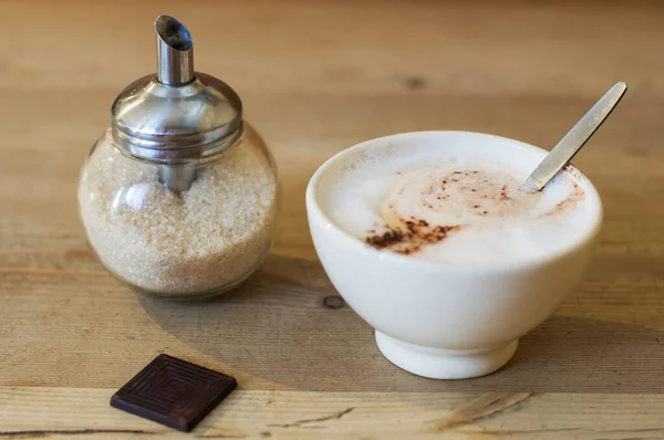a cup of cappuccino and a sugar bowl with a dispenser on a table in a cafe. High quality photo