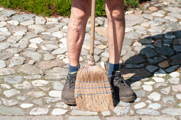 gardener in dirty work clothes and boots holds garden tools, plastic brush broom, seasonal spring work in the garden. High quality photo