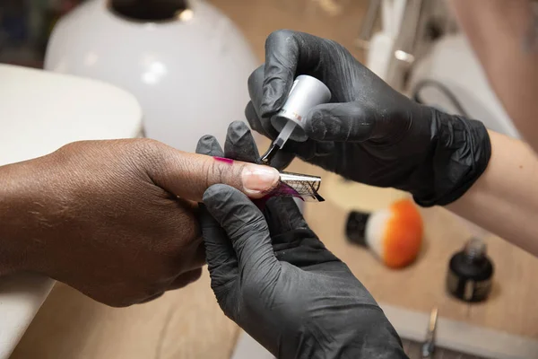 Manicurist doing nail extensions to dark-skinned girls in a beauty salon. High quality photo