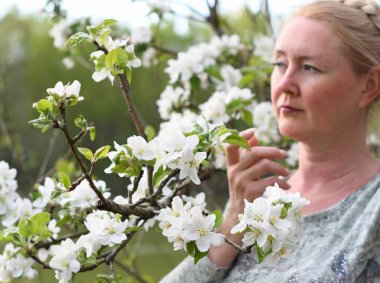 middel aged woman stands in the park next to a flowering tree, Spring time, Adult with blond hair, Wellness concept. High quality photo