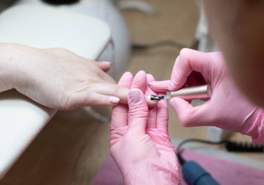 a master does a manicure to a client in a beauty salon and covers her nails with pink varnish. High quality photo