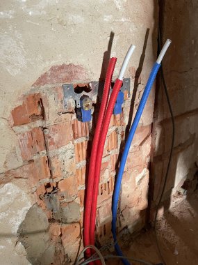 Kablolu kırmızı ve mavi kıvrımlı borular alçı bir duvardan çıkıyor. Tamirat sırasında elektrik dağıtımı. Aşırı ısınma ve soğutma. Yüksek hızlı veri transferi. Yüksek kaliteli fotoğraf.