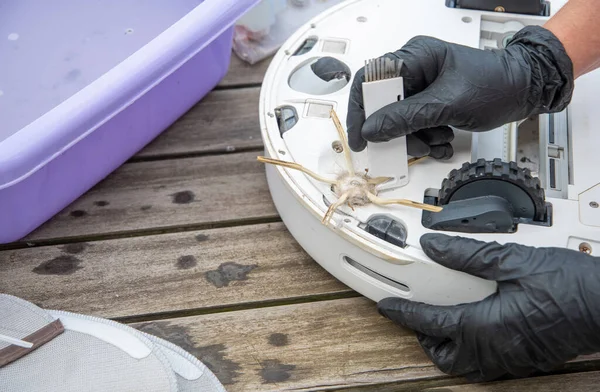 stock image a woman cuts tangled hair with a knife on a brush with three side processes at a vacuum cleaner robot, routine maintenance of equipment for long-term use, high quality photo