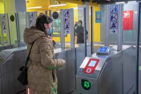暖かいコートを着た衛生マスクの若い女性が地下鉄のターミナルでカードをスキャンしてホームを出る彼女の前でドアをスライドさせます 高品質の写真 — ストック写真