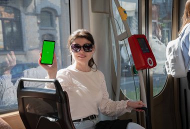 brunette woman showing smartphone with vertical green screen in tram, next to the digital checkout High quality photo
