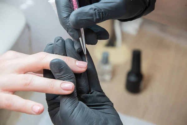 a master does a manicure to a client in a beauty salon and covers her nails with pink varnish, the master levels the edge of the varnish with a thin brush, High quality photo