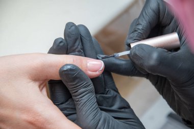 a master does a manicure to a client in a beauty salon and covers her nails with pink varnish. High quality photo
