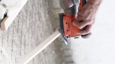 İnşaatçı erkek, yumrulardan çıkan zımpara kağıdıyla odun öğütüyor. Yakın görünüm, ahşap kirişi öğütülmüş, yüksek kaliteli dikey 4k görüntü ile işliyor