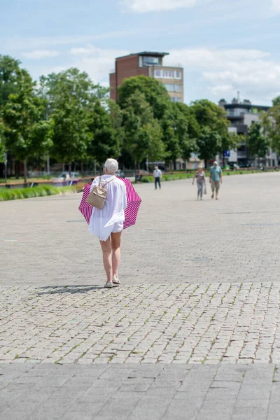 middle-aged woman with a short haircut with an umbrella protecting from the scorching sun is looking for something in her handbag, High quality photo