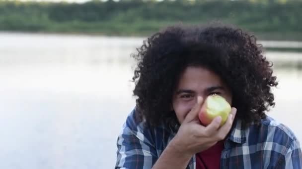 幸せな黒髪のカーリーハンサム驚いたアラブの男はリンゴを噛んで笑い 彼のまっすぐな白い歯を示し カメラを見て 高品質のフルHd映像 — ストック動画