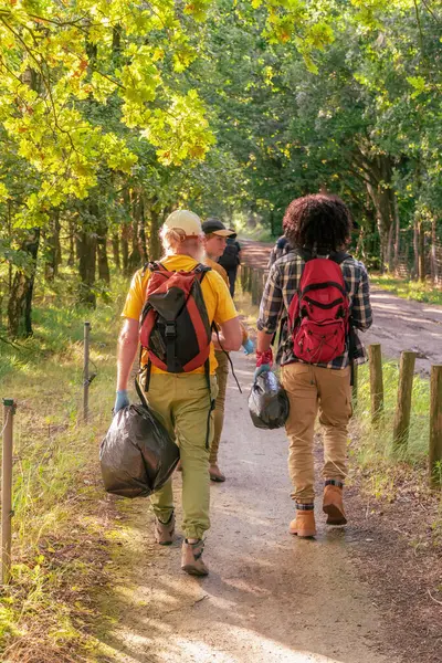 group of volunteer tourists dressed in comfortable hiking clothes walk together in the forest to collect garbage, carrying swords and gloves,the concept of ecology and cleanliness,High quality photo