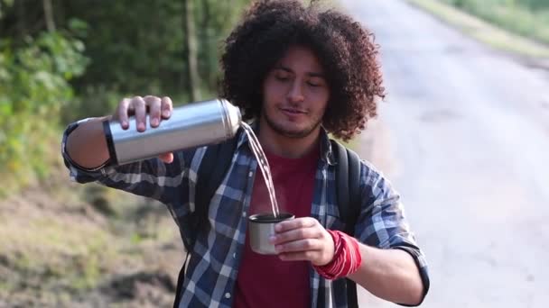若い黒髪のアラブ人男性が熱湯からマグカップに沸騰し 森林を背景に熱いお茶を散歩しています 高品質のフルHd映像 — ストック動画