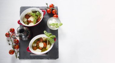 İtalyan caprese salatası, fırında kiraz domatesleri, beyaz bir masada mozzarella ve fesleğen, durgun hayat, düz yatak, kopyalama alanı