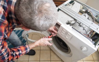Kareli takım elbiseli orta yaşlı usta bir çamaşır makinesinin kapağını tamir için bir tornavidayla açıyor, evde çamaşır makineleri ve ev aletleri tamir ediyor, yüksek kaliteli fotoğraf çekiyor.