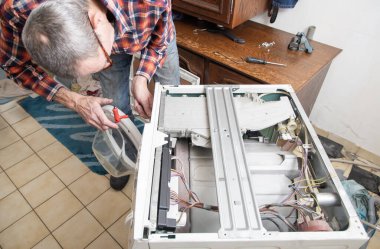 Kareli takım elbiseli orta yaşlı usta bir çamaşır makinesinin kapağını tamir için bir tornavidayla açıyor, evde çamaşır makineleri ve ev aletleri tamir ediyor, yüksek kaliteli fotoğraf çekiyor.