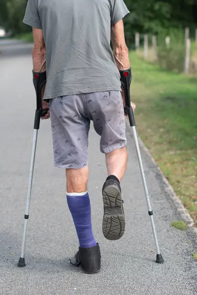 A man with a broken leg is walking down the street, on his left leg he has a special boot for walking, if the leg is in a cast, the man moves with the help of crutches,high quality photo