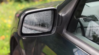 Yağmurdan hemen sonra arabanın sol tarafındaki aynayı kapat, kadın kapıyı açar, direksiyonun başına geçer ve aynayı silmek için pencereyi indirir, seçici odak noktası, 4K 'daki yüksek kaliteli çekim.