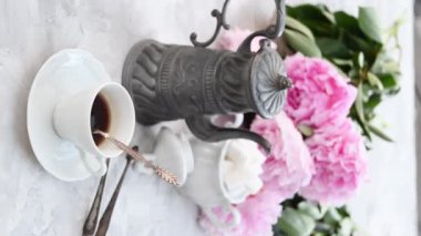 Kadınların elleri espresso kahveyi karıştırıyor ve porselen bir fincana porselen bir fincana, masanın üzerinde pembe şakayık desenleri olan yüksek kaliteli 4K görüntüler ekliyor.