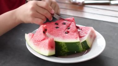 Childs bir parça karpuz hamurunu masa bıçağıyla keser, masada olgun kırmızı karpuz parçaları, yazın sulu tatlı, vitaminli meyve diyeti