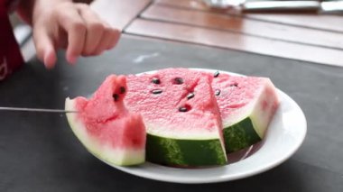 Childs bir parça karpuz hamurunu masa bıçağıyla keser, masada olgun kırmızı karpuz parçaları, yazın sulu tatlı, vitaminli meyve diyeti