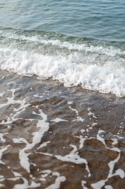 Gün batımında deniz kıyısında küçük köpüklü dalgalar gelir ve gider. Yaz tatilinde hoş bir tatil, dinlenme, dalgaların sesine doğru bir yürüyüş, yüksek kaliteli dikey fotoğraf.