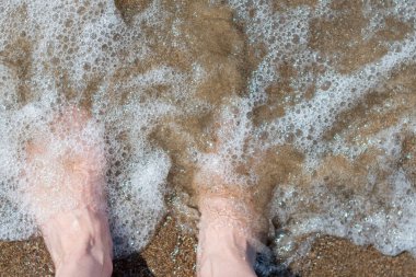 Bir yaz günü kumlu bir plajda çıplak ayakla çıplak ayak, kadın ayaklarının en üst görüntüsü, sıcak deniz suyunda ayaklarını ıslatan kadın, deniz kenarında kaygısız bir tatil., 