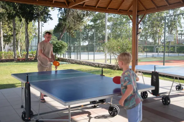 stock image eight year old blond boy plays ping pong with his father on a special table tennis court, fun summer sports activities for children, unforgettable summer holidays with the whole family in Turkey