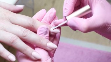 Pembe koruyucu eldivenli manikürcü, beyaz bir kadının sağ elinin işaret parmağındaki güzel uzun tırnakları kaplıyor. Sağlığına ve güzelliğine dikkat ediyor.