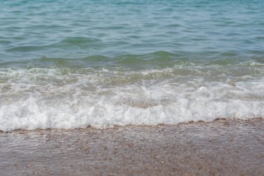 Gün batımında deniz kıyısında küçük köpüklü dalgalar gelir ve gider. Yaz tatilinde hoş bir tatil, dinlenme, dalgaların sesine doğru bir yürüyüş, yüksek kaliteli yatay fotoğraf.