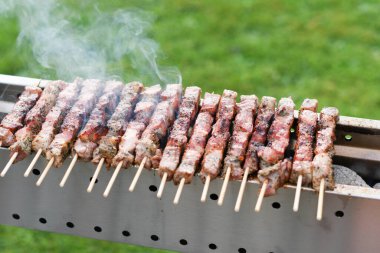 Genç bir adam kömürde et kebabı pişiriyor, ARROSTICHINI - tipik güney İtalyan mutfağı, yazın evin yakınındaki terasta lüks bir piknik, barbekü üzerinde aromatik dumanlar yükseliyor.,