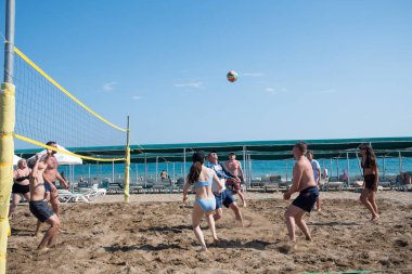 Turistler tatil sırasında denizde plaj voleybolu oynarlar, top açık mavi gökyüzüne doğru uçar ve 31 Mayıs 2024 'te Belek, Türkiye' deki Yeşil Max Oteli 'nin plajında dinlenir..