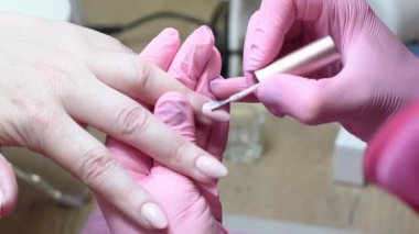 Pembe koruyucu eldivenli manikürcü, beyaz tenli bir kadının sol elinin yüzük parmağındaki güzel, uzun tırnakları kaplıyor. Sağlığına ve güzelliğine dikkat ediyor.